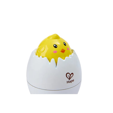 A white toy egg with a cartoonish yellow chick hatching from it, with the brand Hape visible on the egg.