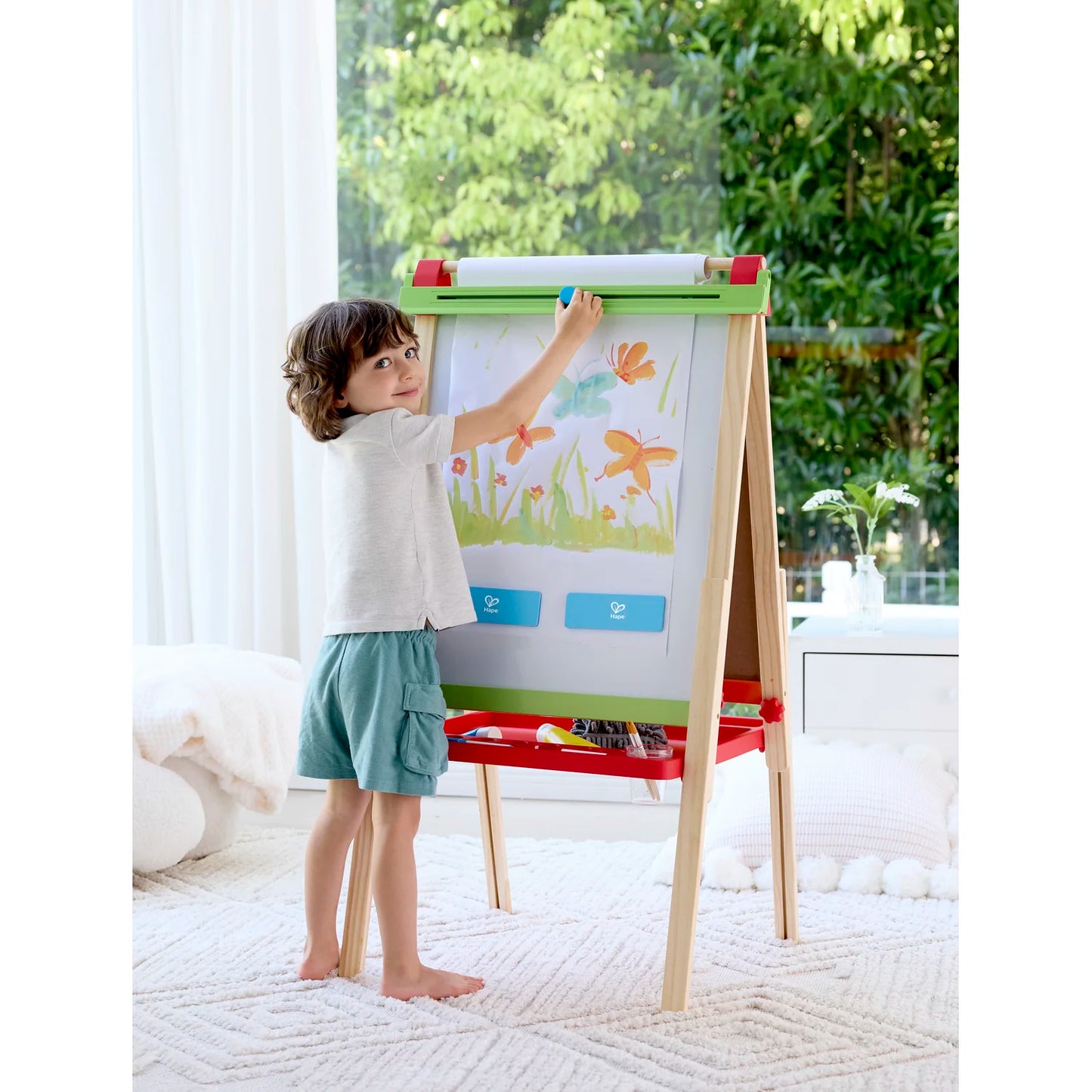 Child drawing on a colorful easel in a bright room with plants in the background