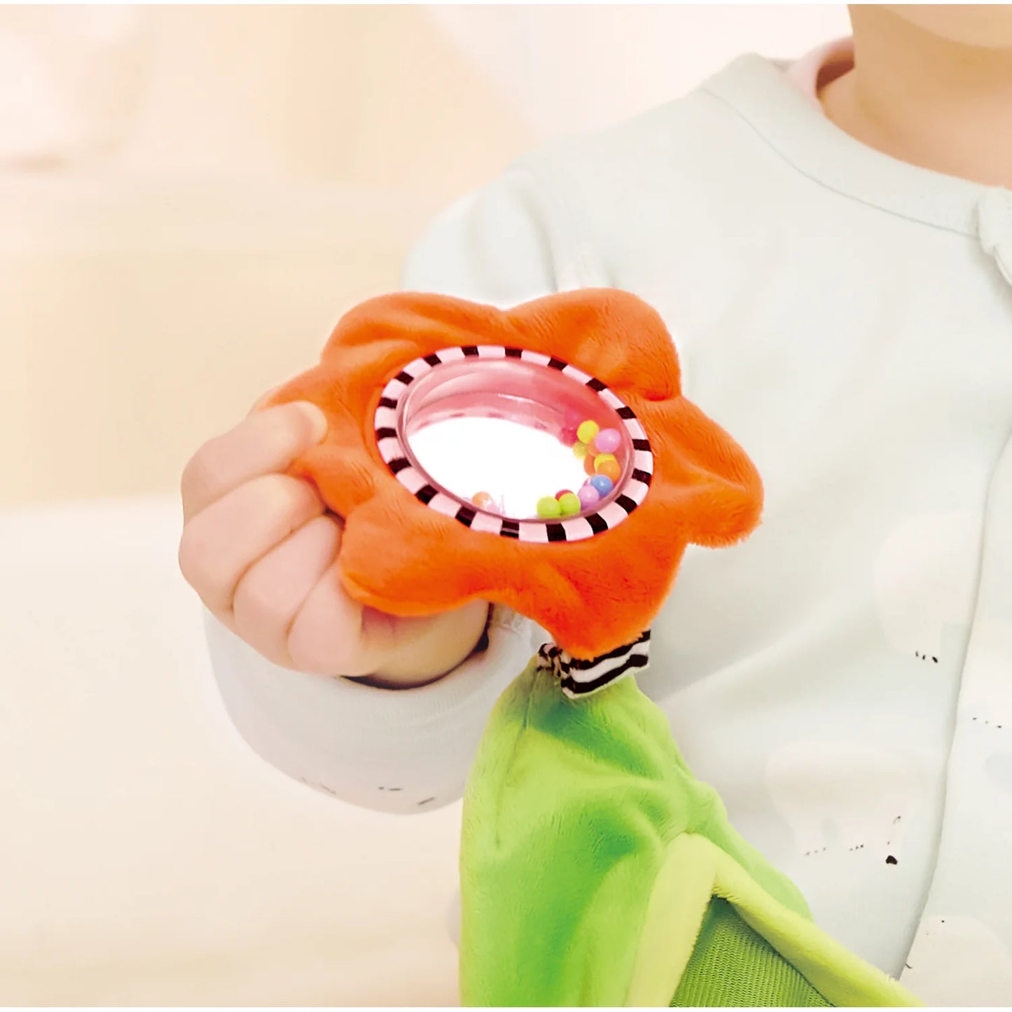 Baby hand holding an orange flower-shaped toy with a mirror
