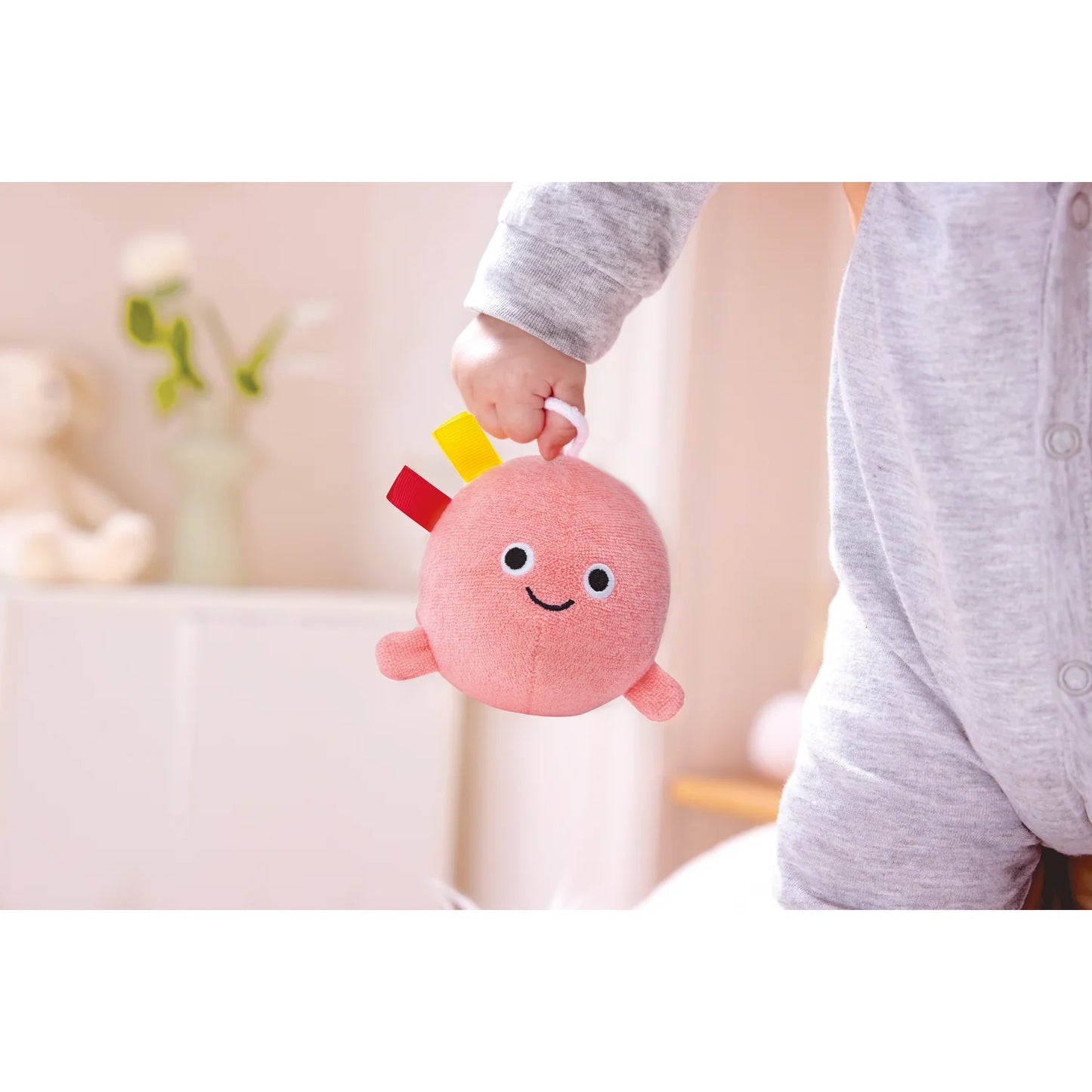 Child holding a pink plush toy with a smiley face against a blurred indoor background