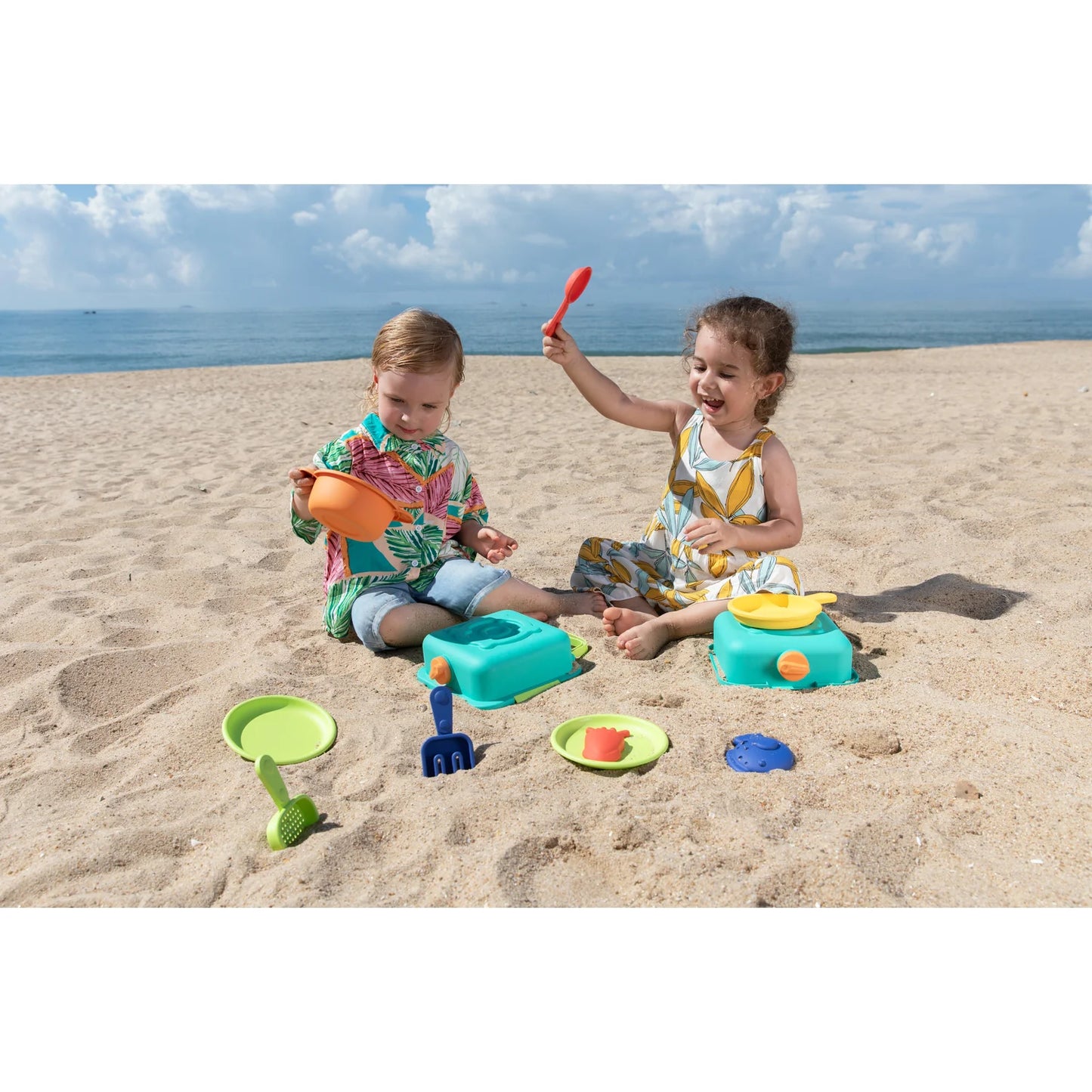 Two children playing with beach toys on a sandy beach with ocean in the background