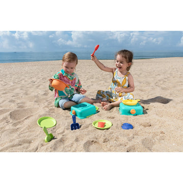 Two children playing with beach toys on a sandy beach with ocean in the background