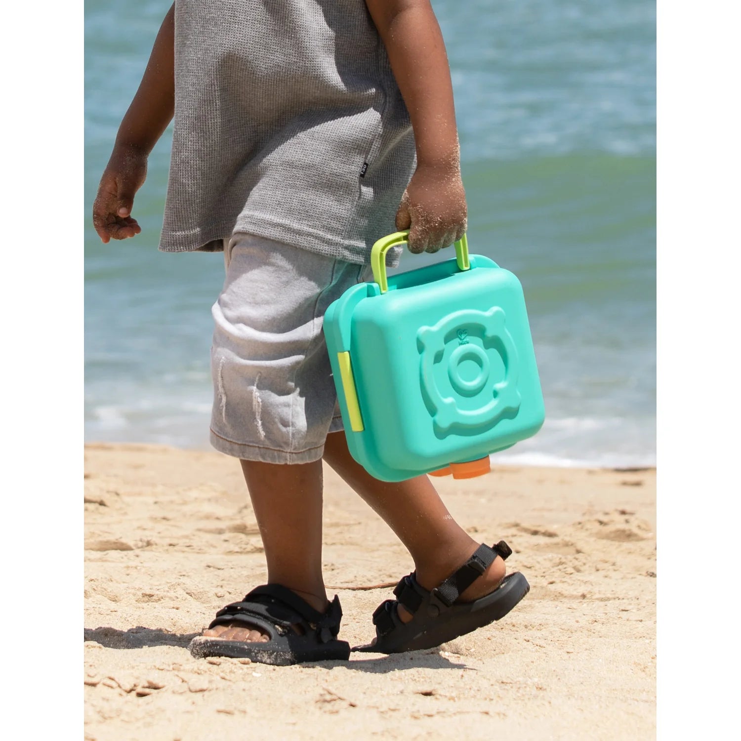 Child holding a teal toy camera on a beach