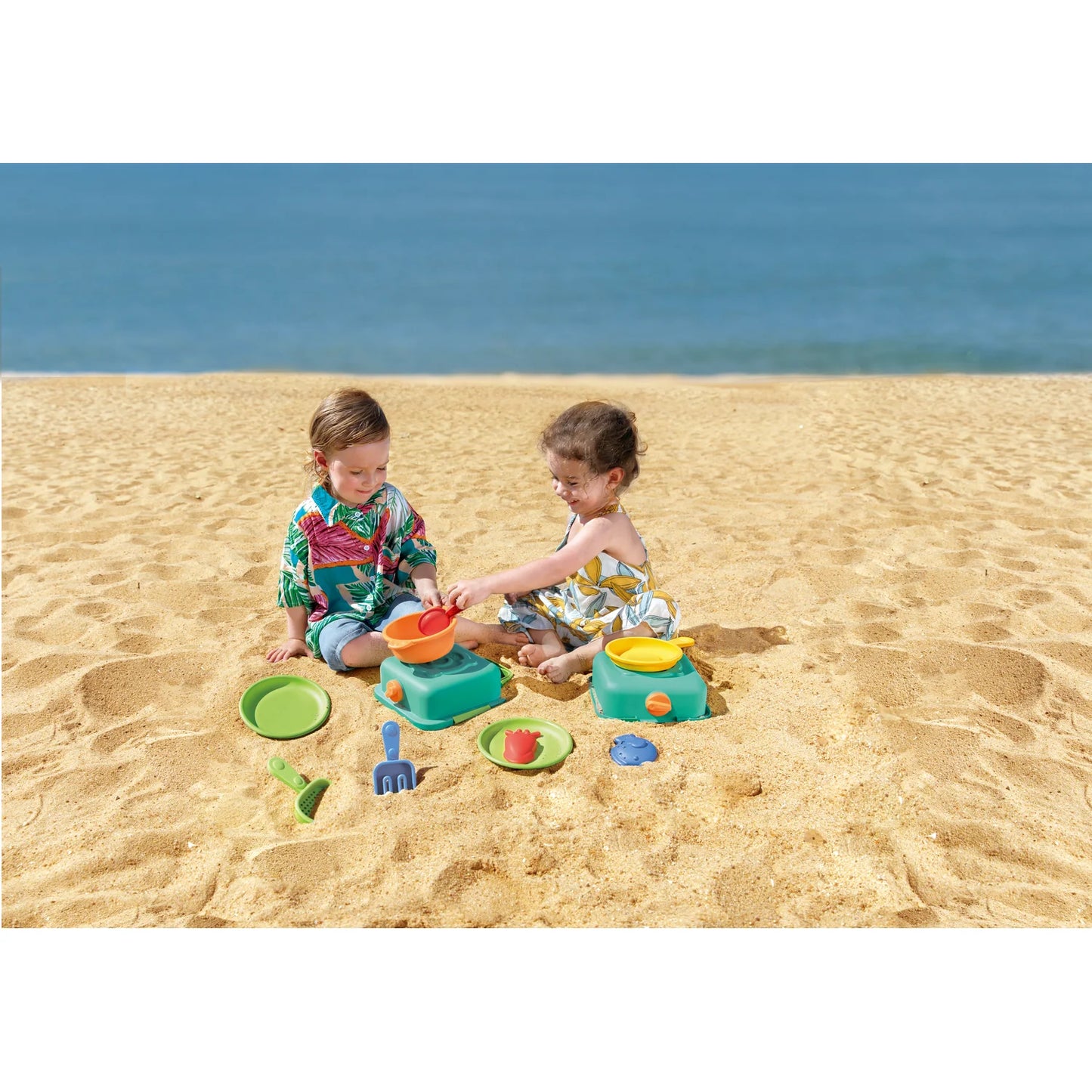 Two children playing with colorful sand toys on a sandy beach.