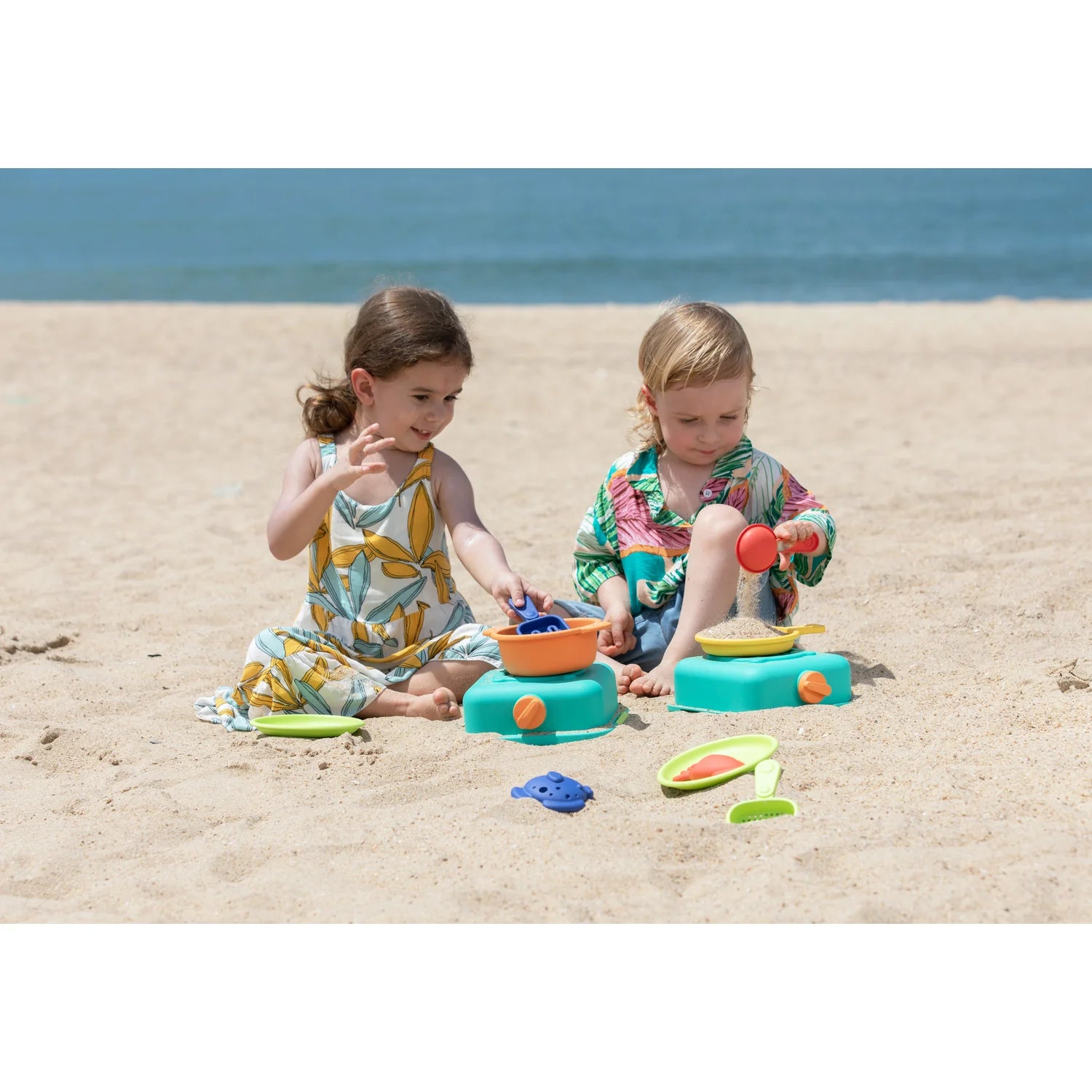 Two children playing with colorful sand toys on a sandy beach.