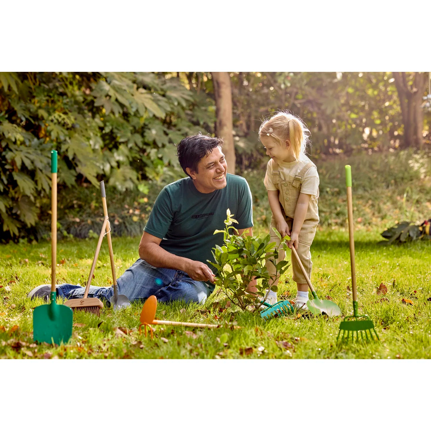 Man and child gardening together in a park with gardening tools around them.