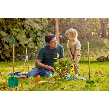 Man and child gardening together in a park with gardening tools around them.