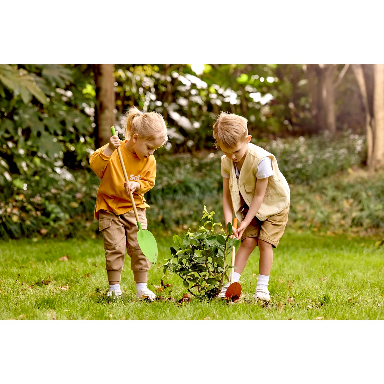 Two children planting a tree in a grassy area with trees in the background