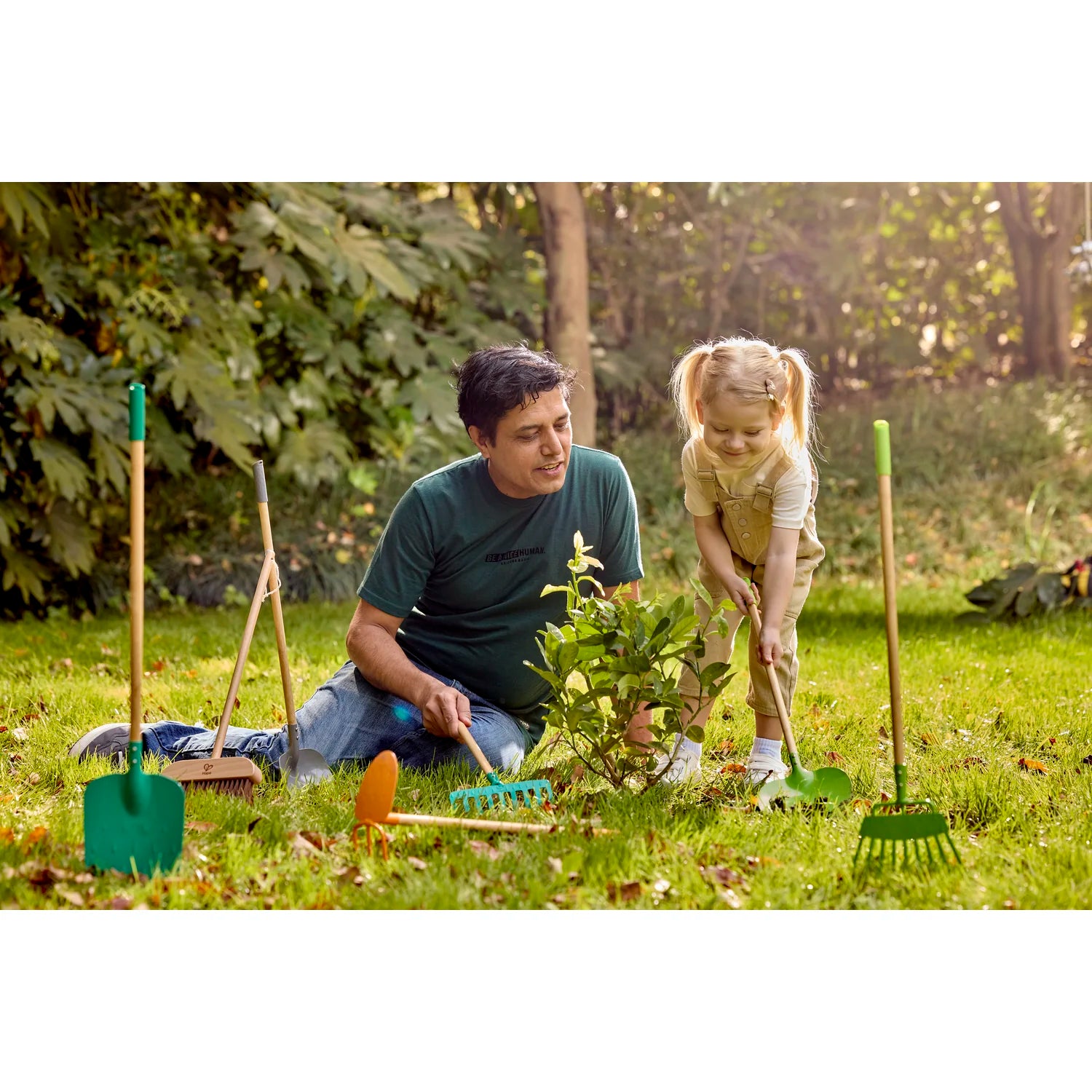 Man and young girl gardening together in a backyard with gardening tools around them.