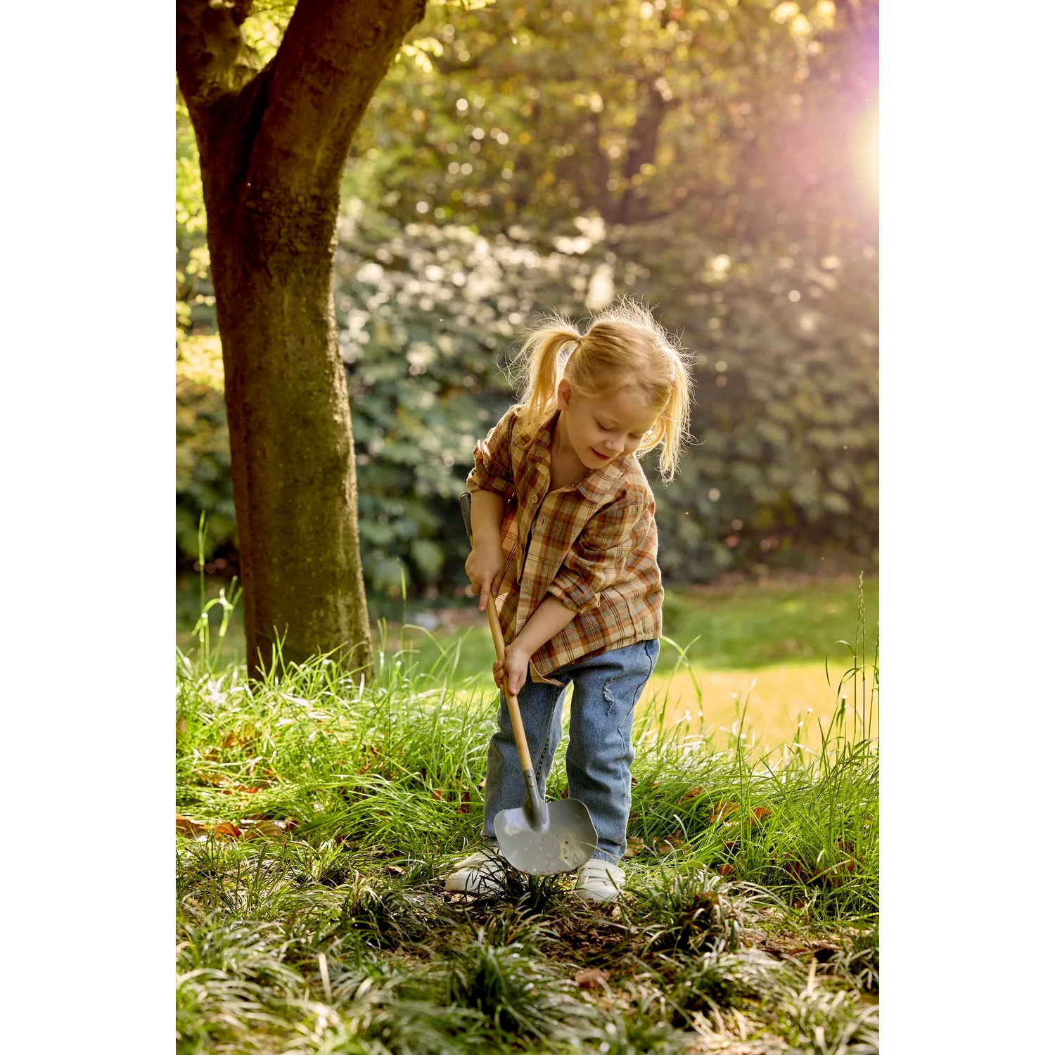 Child playing with a shovel in a grassy area with trees