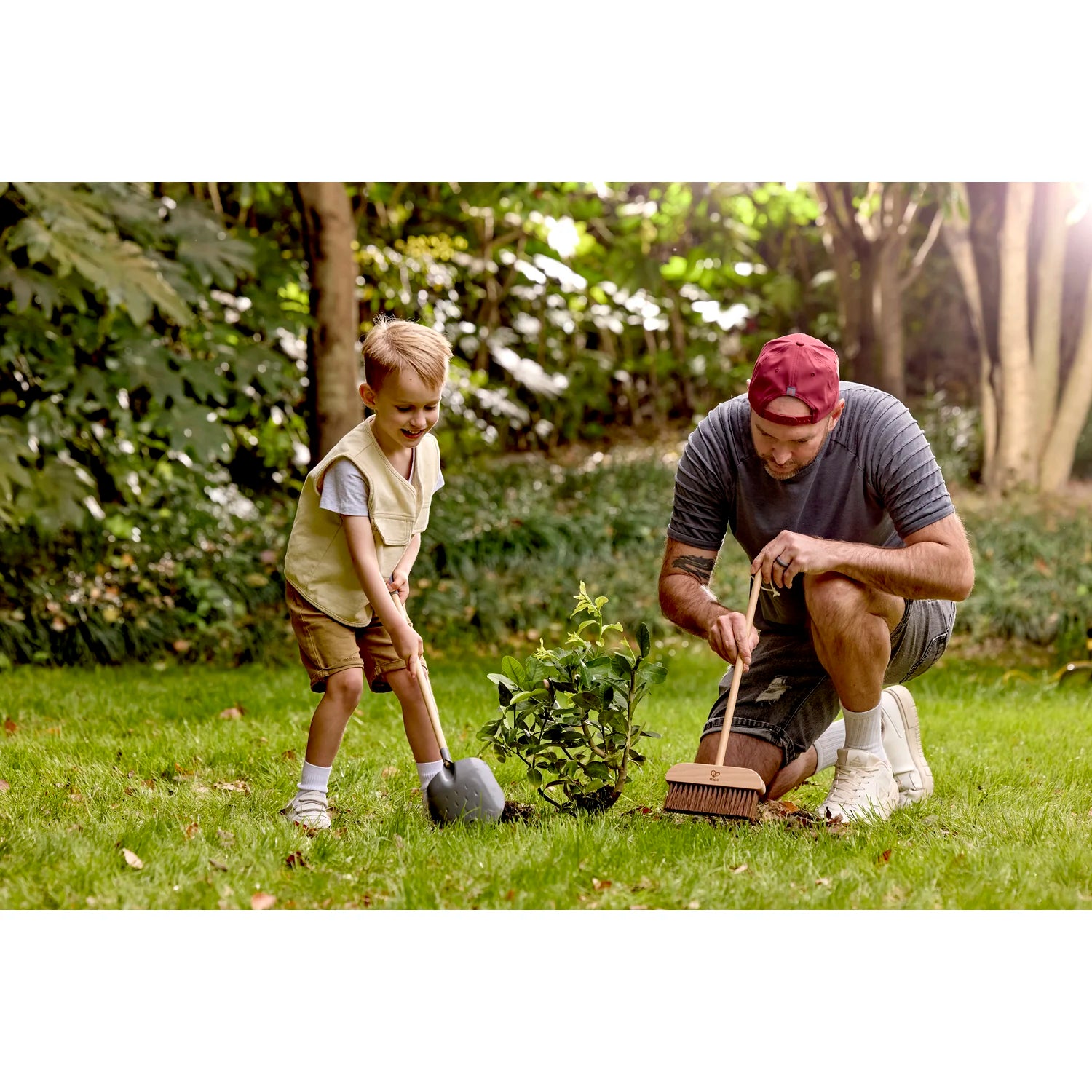 Man and child gardening together in a park with trees and grass in the background