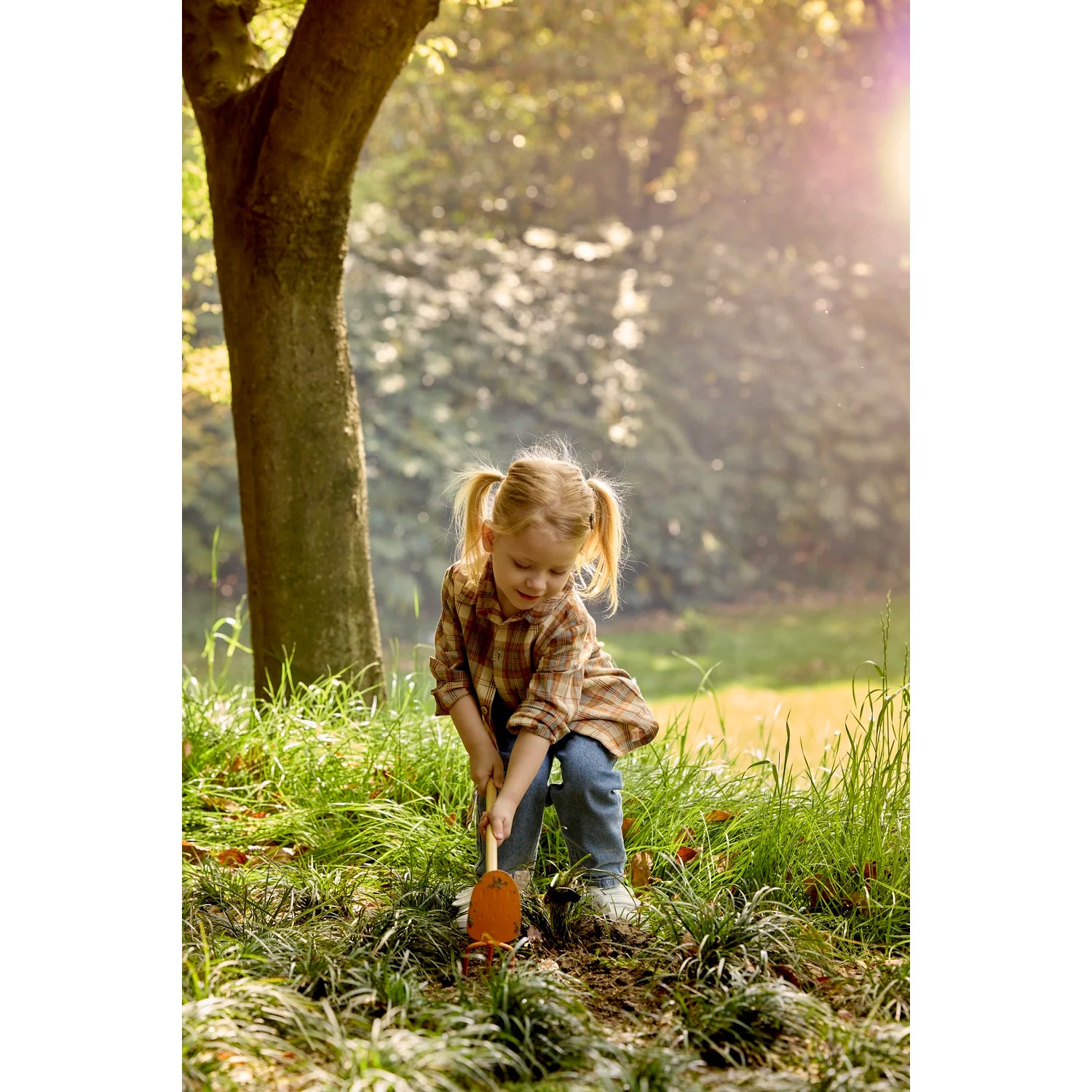 Child playing with a shovel in a grassy area with trees in the background