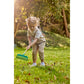 Child in a garden using a green rake on a grassy area with trees in the background.