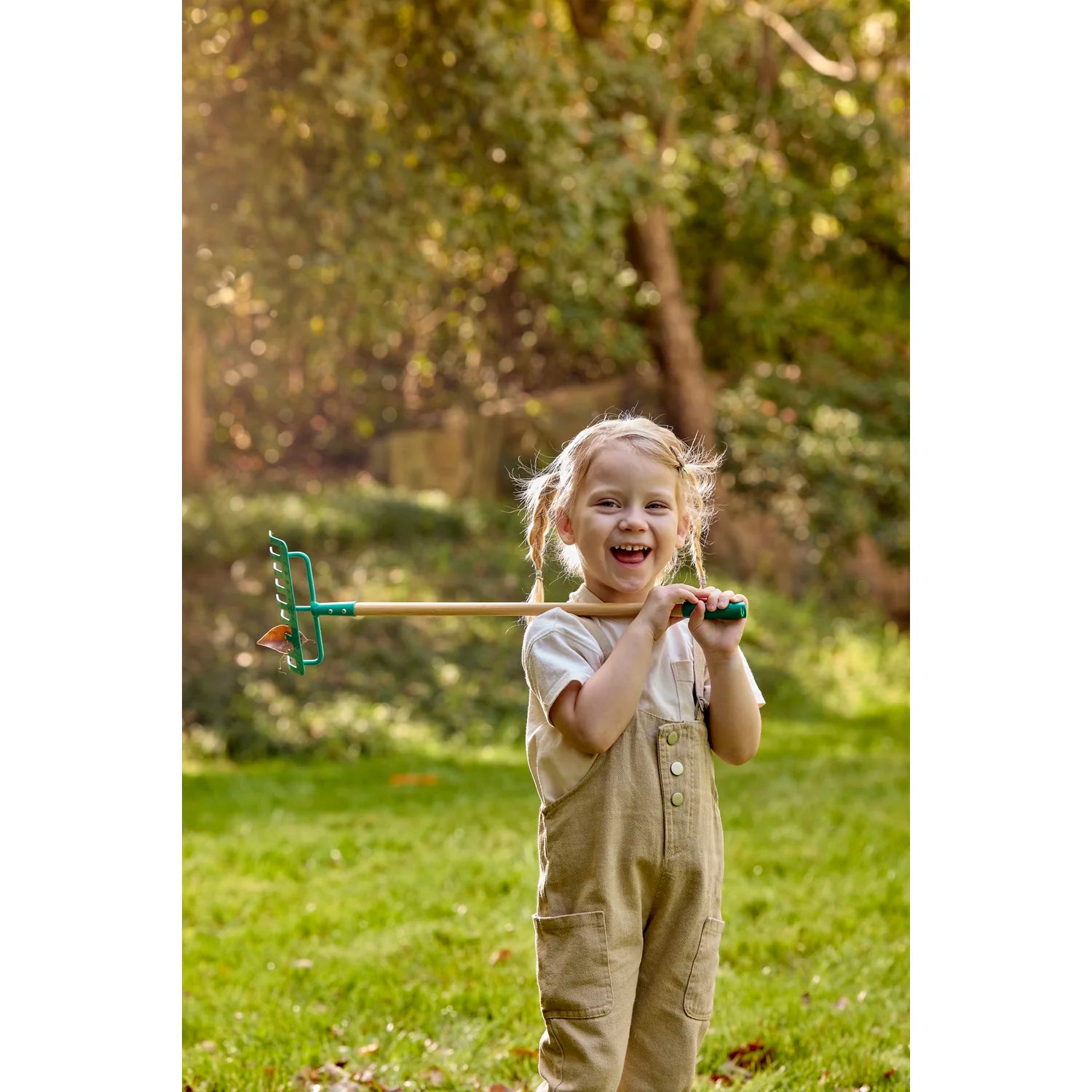 Child holding a garden rake in a grassy outdoor setting