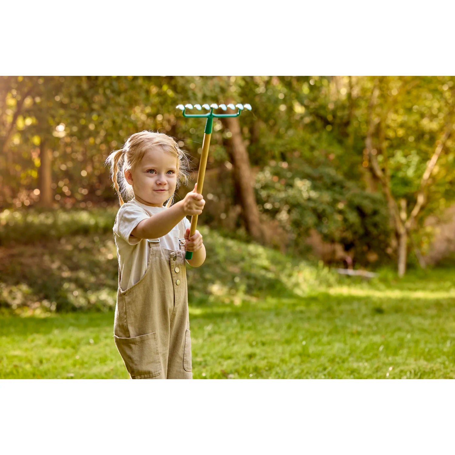 Child holding a garden rake in a grassy outdoor setting