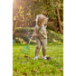 Child playing with a green garden rake in a grassy area with trees in the background