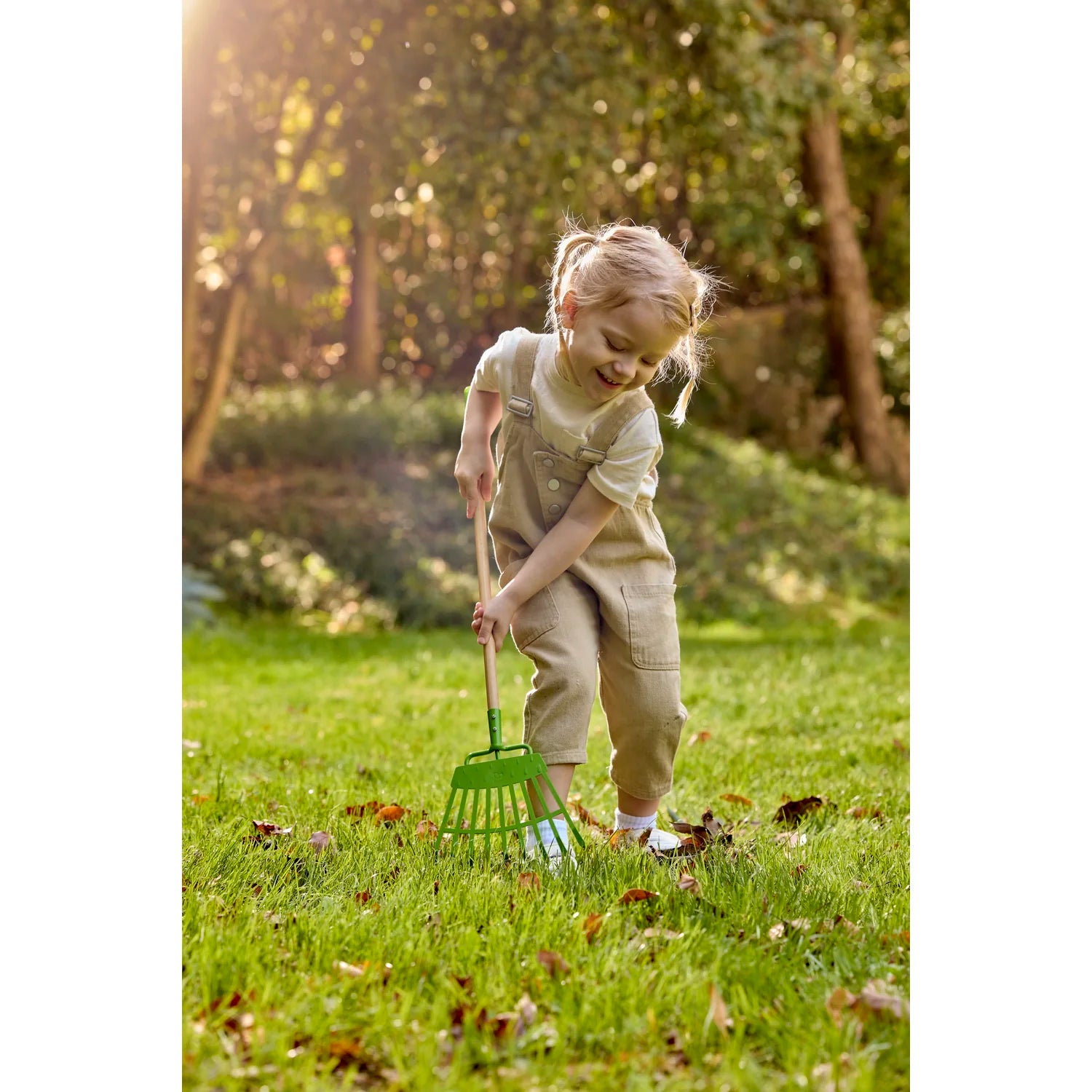 Child playing in a garden with a green tool, surrounded by trees and grass.