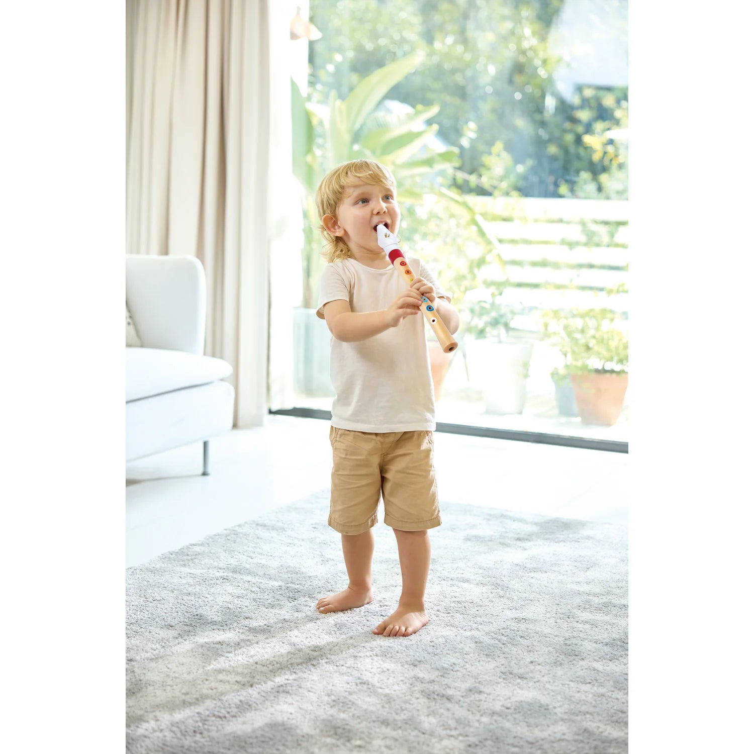 Child playing a recorder in a bright room with large windows