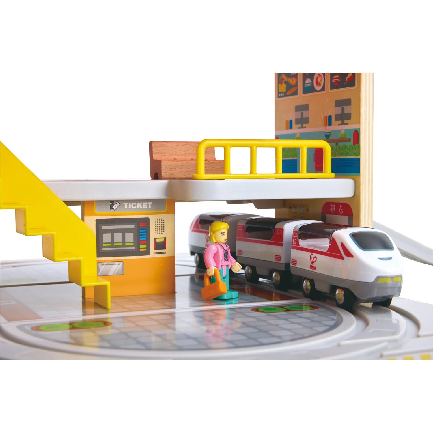 Toy train set with a station and a toy figure near a ticket machine.