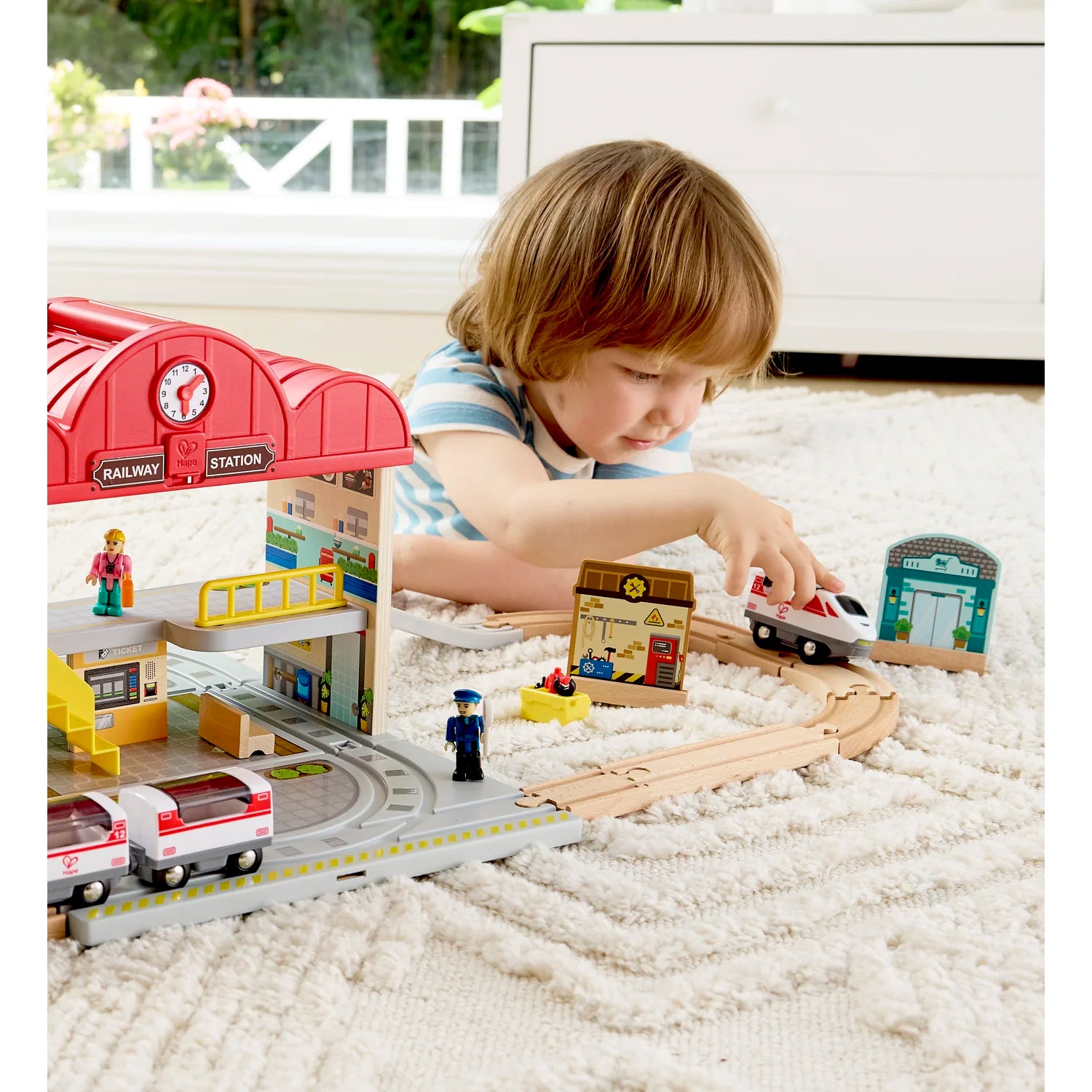 Child playing with a toy train set on a white carpet