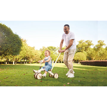Man pushing a child on a tricycle in a park