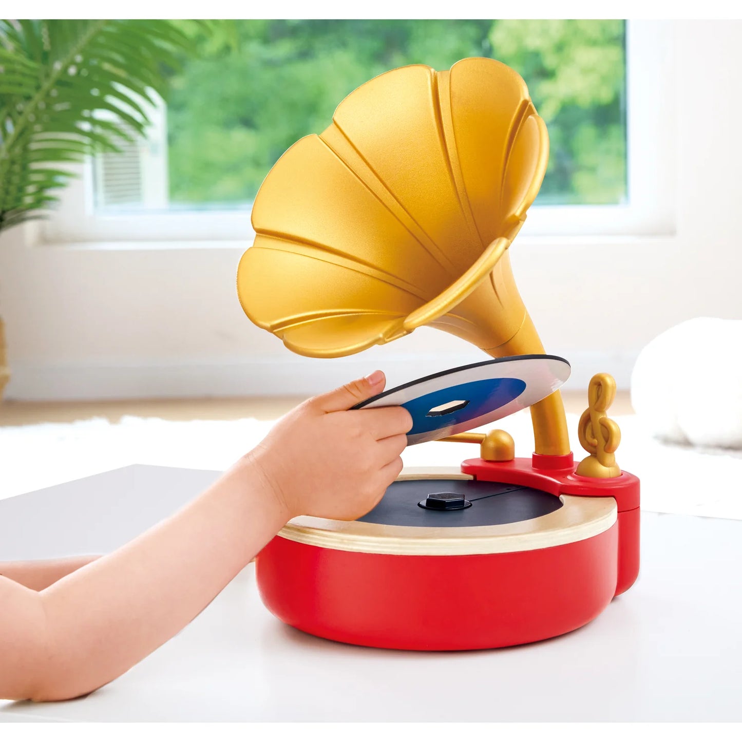 Children's toy resembling a vintage gramophone with a hand interacting with it, set against a bright indoor background.