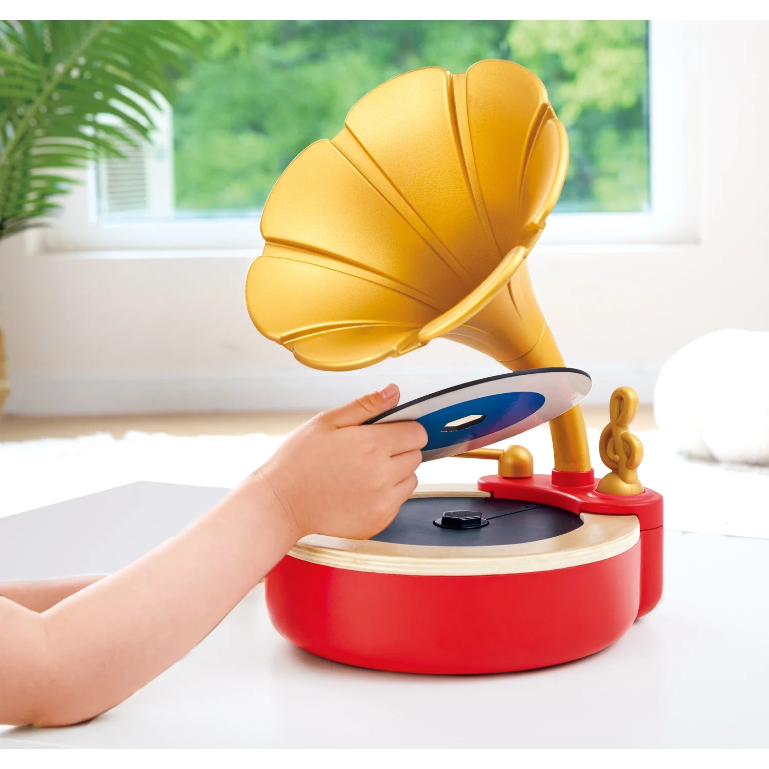 Children's toy resembling a vintage gramophone with a hand interacting with it, set against a bright indoor background.