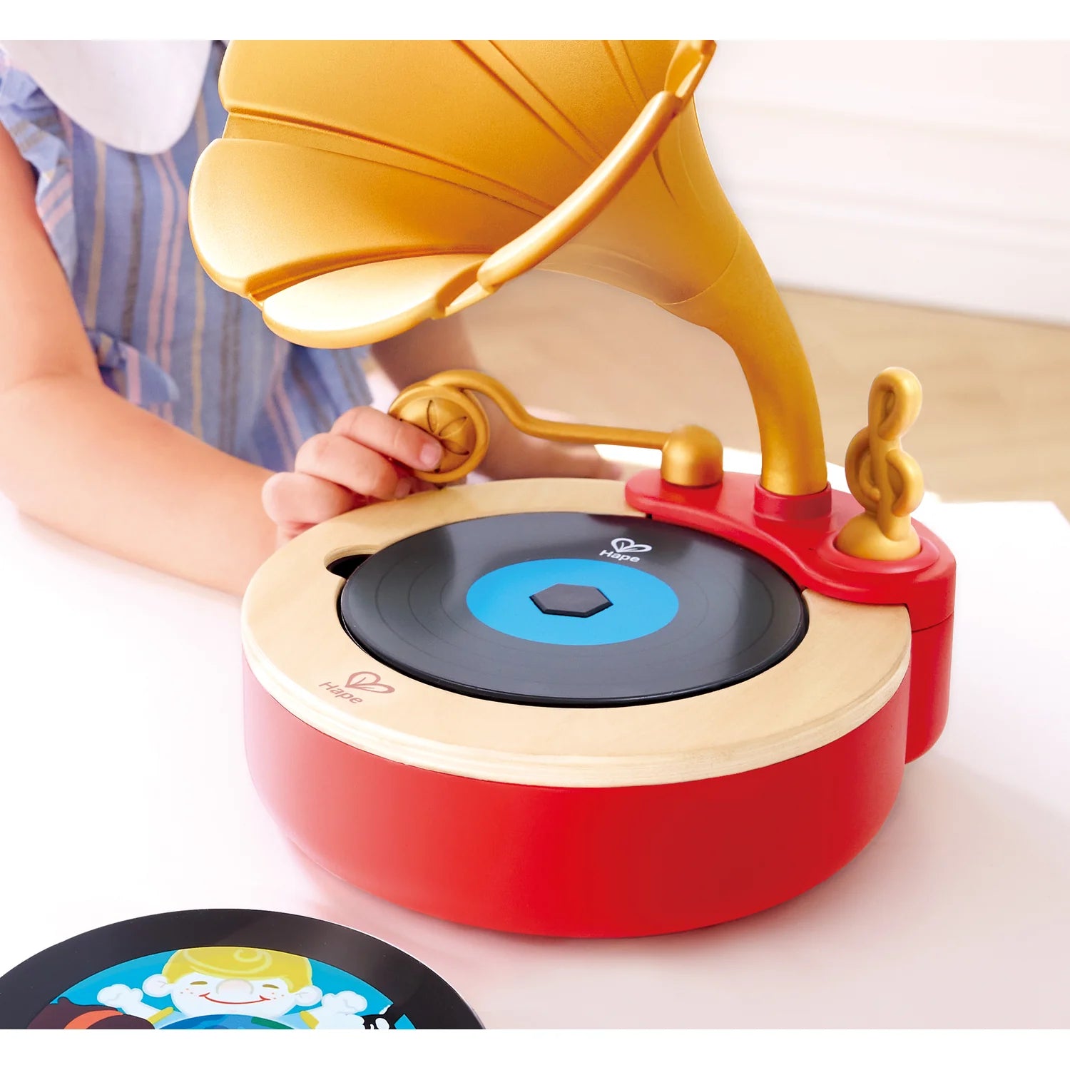 Toy record player with a child's hand interacting with it on a white surface.
