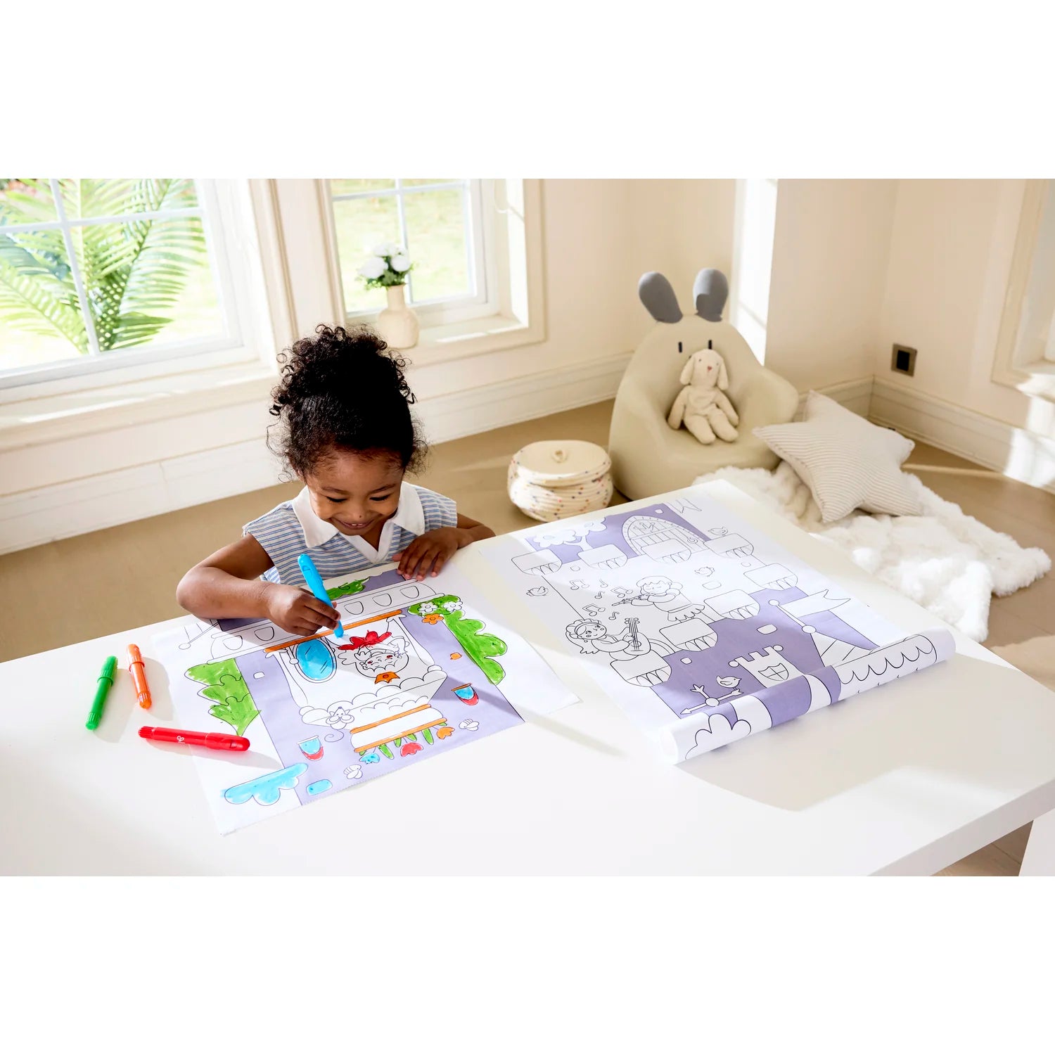 Child coloring at a table with coloring books and markers in a bright room.