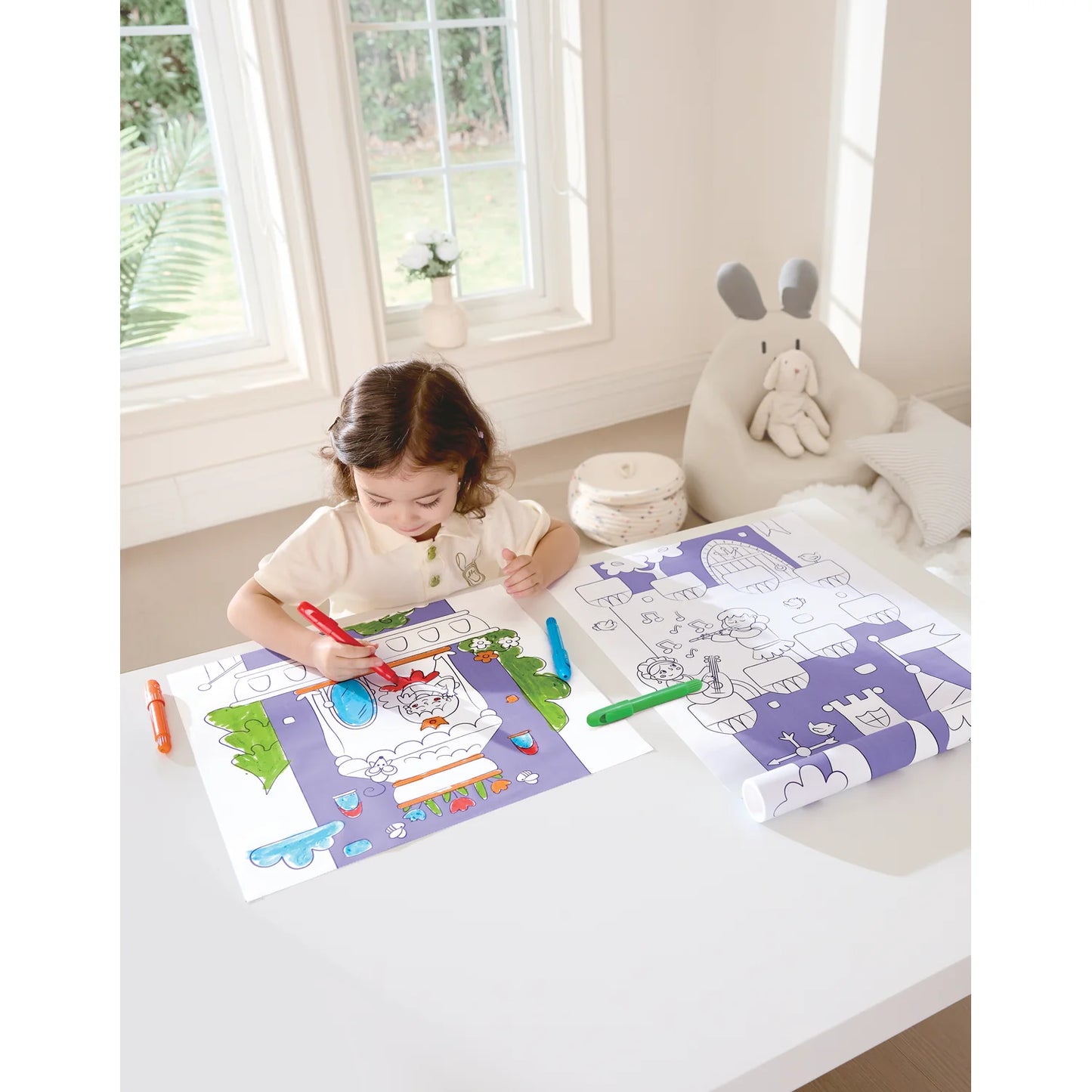 Child coloring on a table with coloring books and crayons in a bright room.