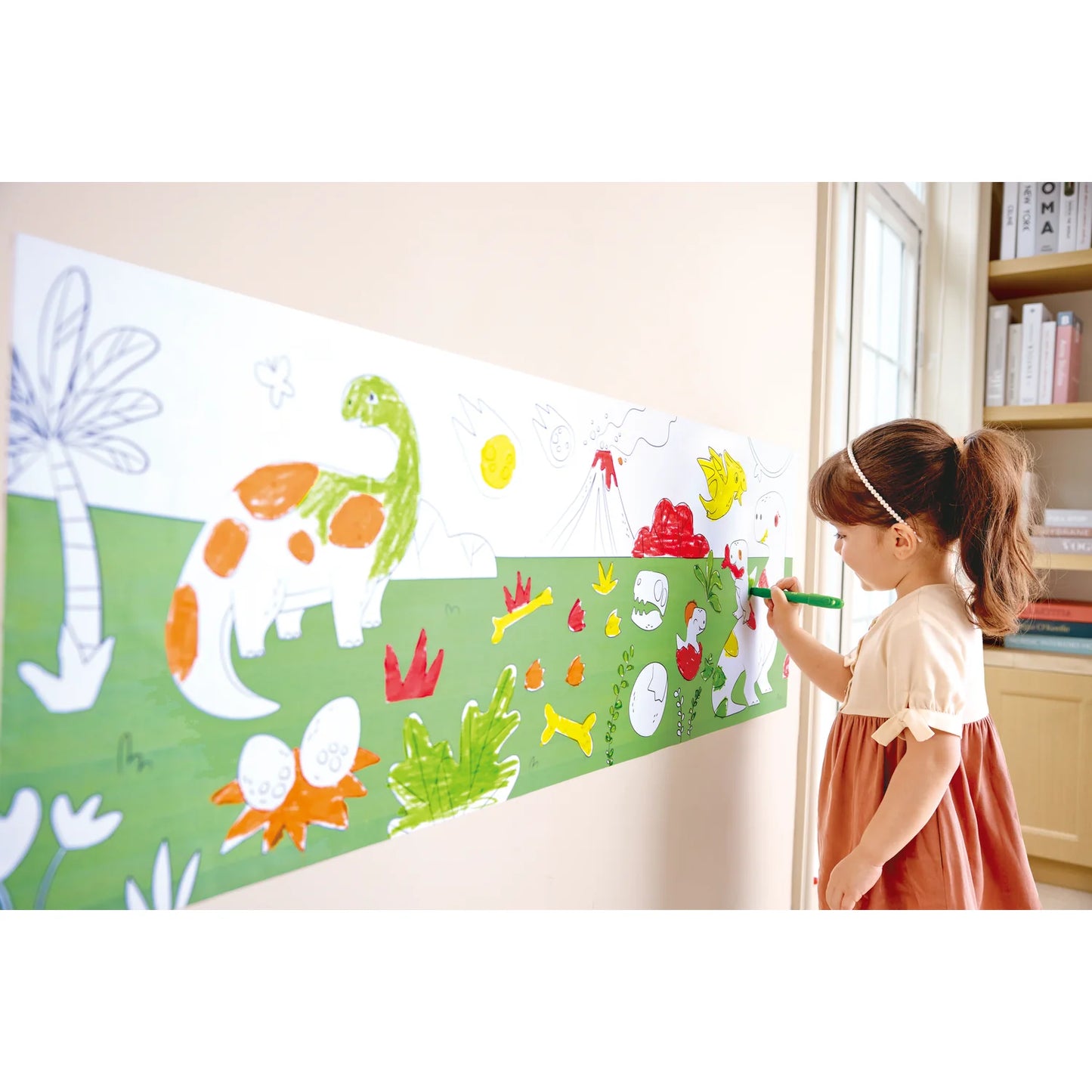 Child drawing on a large paper with dinosaur and plant illustrations in a room.
