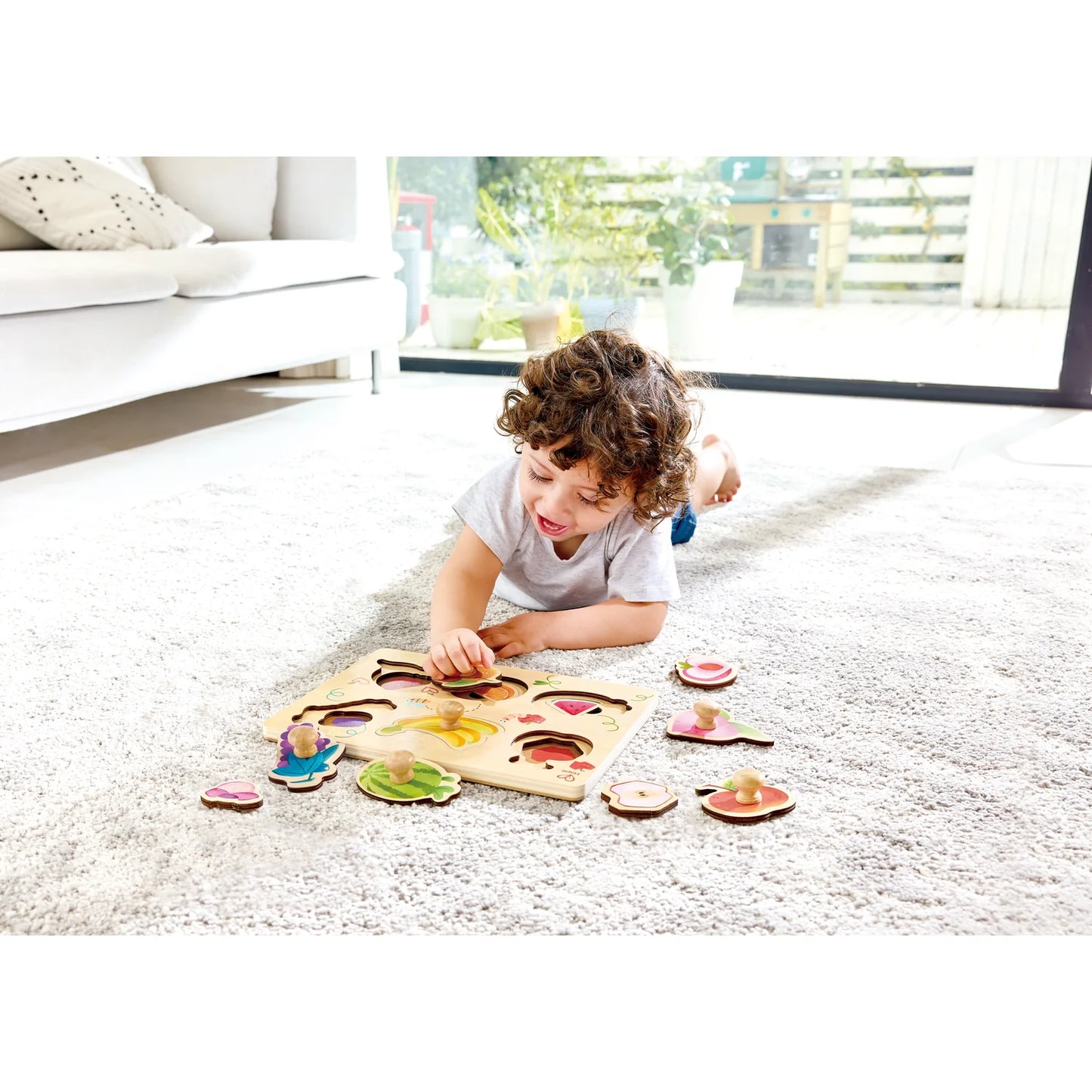 Child playing with a wooden puzzle on a carpeted floor in a living room.