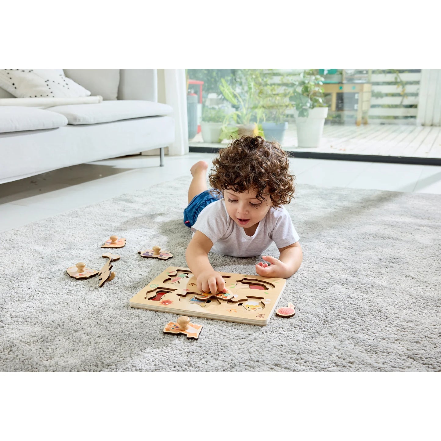 Child playing with a wooden puzzle on a carpeted floor in a living room.