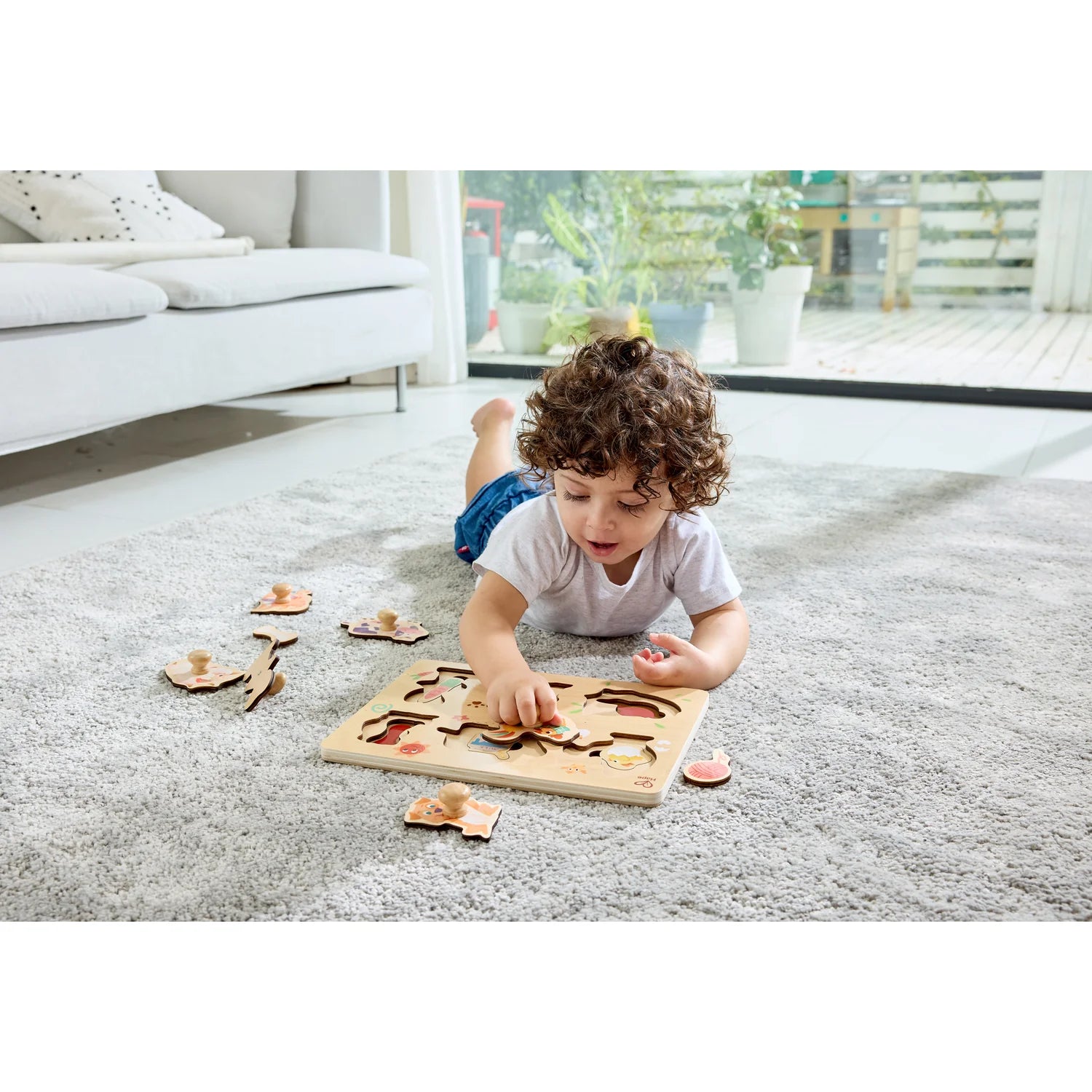 Child playing with a wooden puzzle on a carpeted floor in a living room.