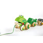 A wooden pull-along toy featuring a green frog with a froglet and a tadpole, connected by rubber-rimmed wheels that won't scratch the floor.