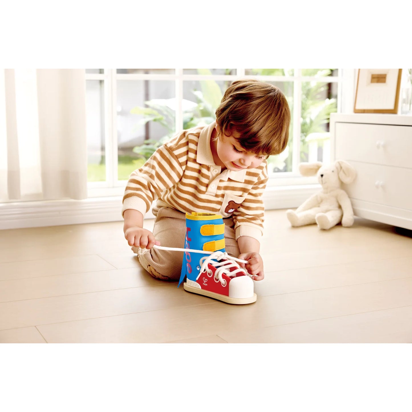 Child playing with a colorful toy shoe on a wooden floor.