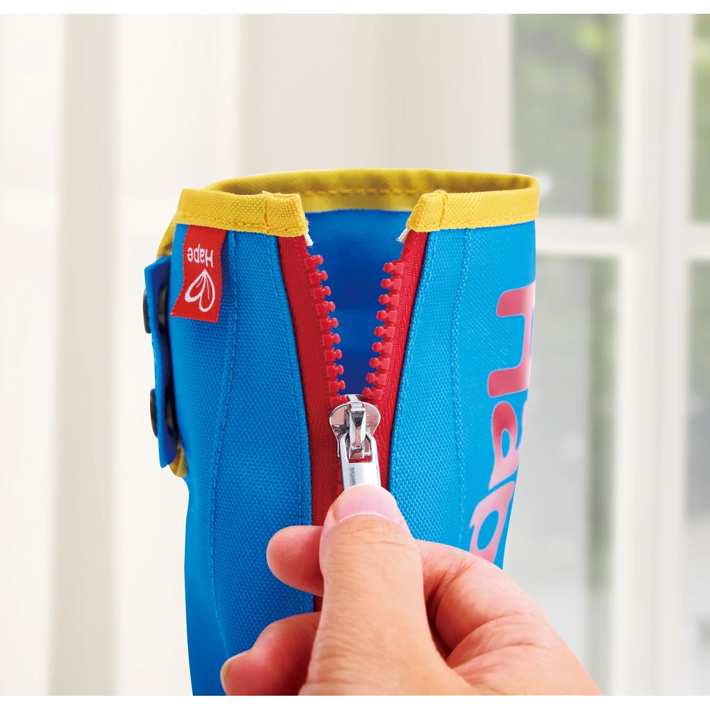 Colorful water bottle holder with a zipper being held by a hand against a blurred window background