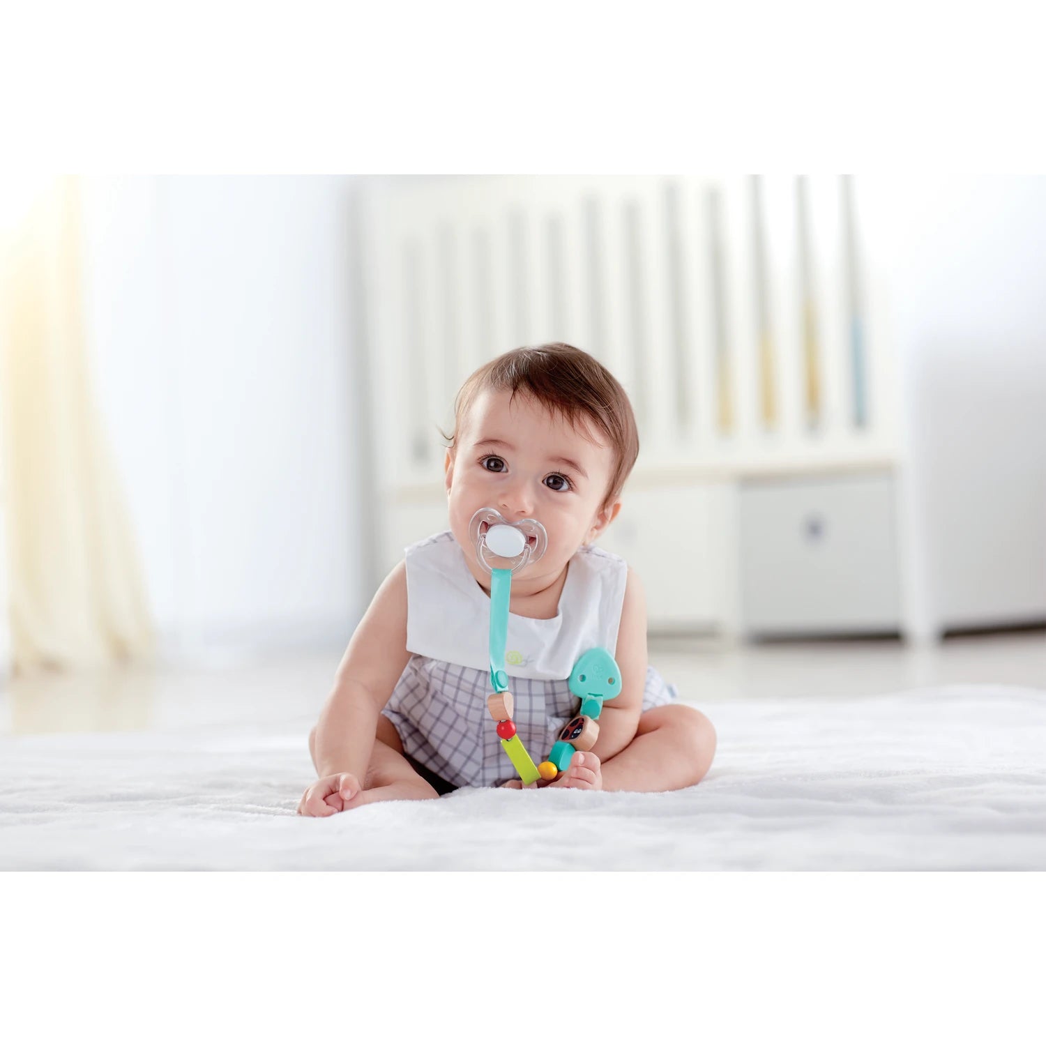 Baby sitting on a bed with a colorful teething ring
