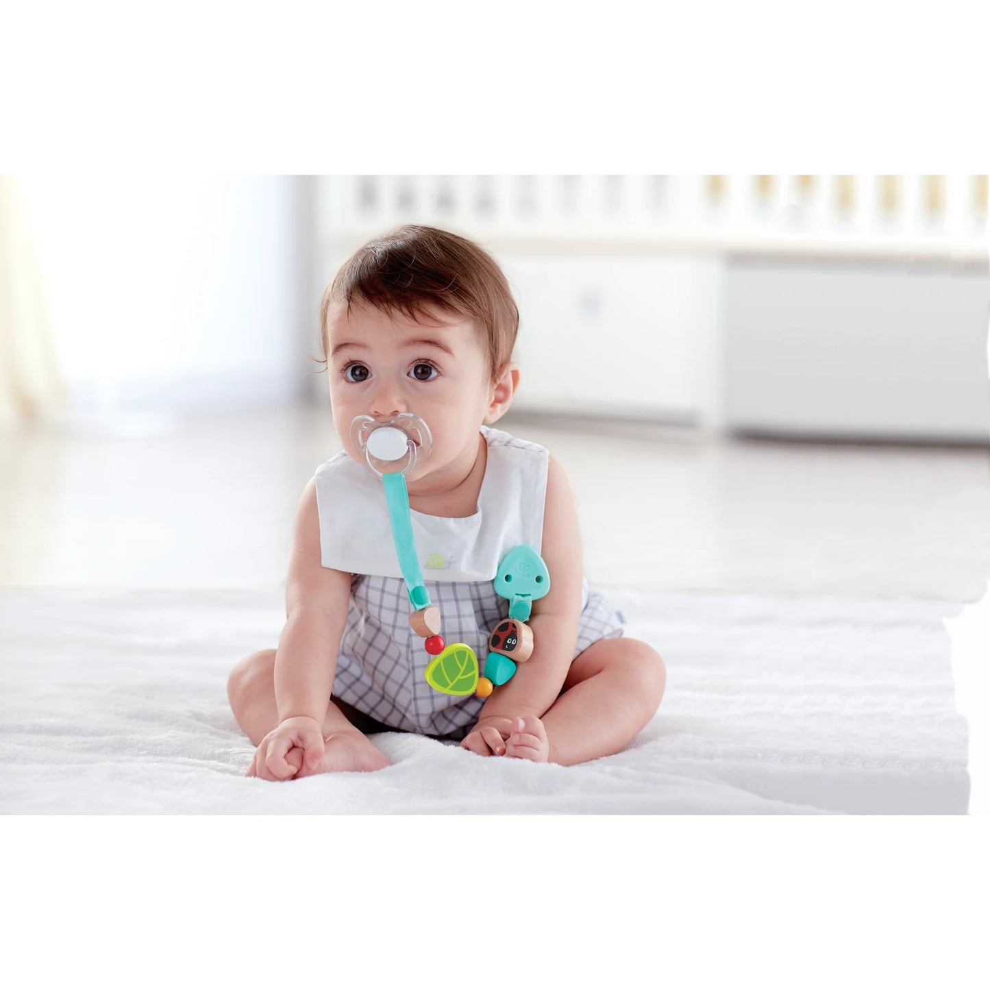 Baby sitting on a bed with a pacifier and colorful toy