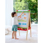 Child drawing on a colorful easel in a bright room with plants in the background