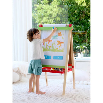 Child drawing on a colorful easel in a bright room with plants in the background