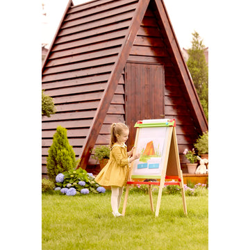 Child painting on an outdoor easel in front of a wooden playhouse