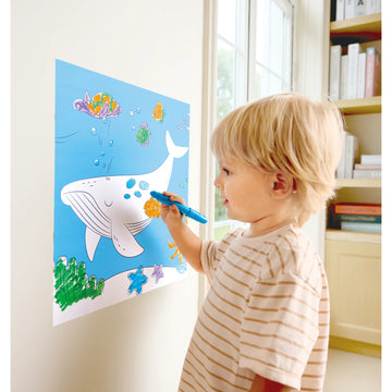 Child drawing on a large paper with a whale and fish illustration, using a blue marker.