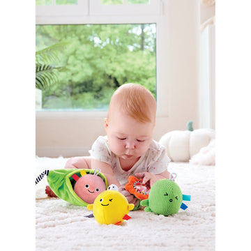 Baby playing with colorful soft toys on a white surface with a window in the background
