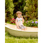 Child sitting in a small boat outdoors with flowers and greenery in the background