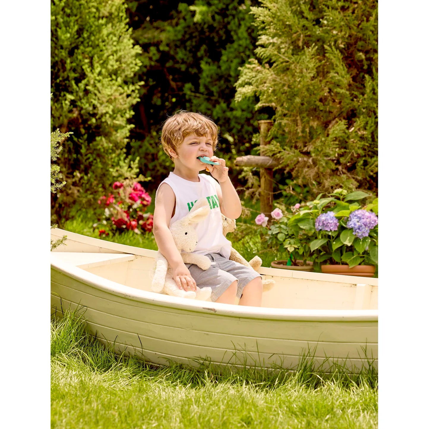 Child sitting in a small boat outdoors with flowers and greenery in the background