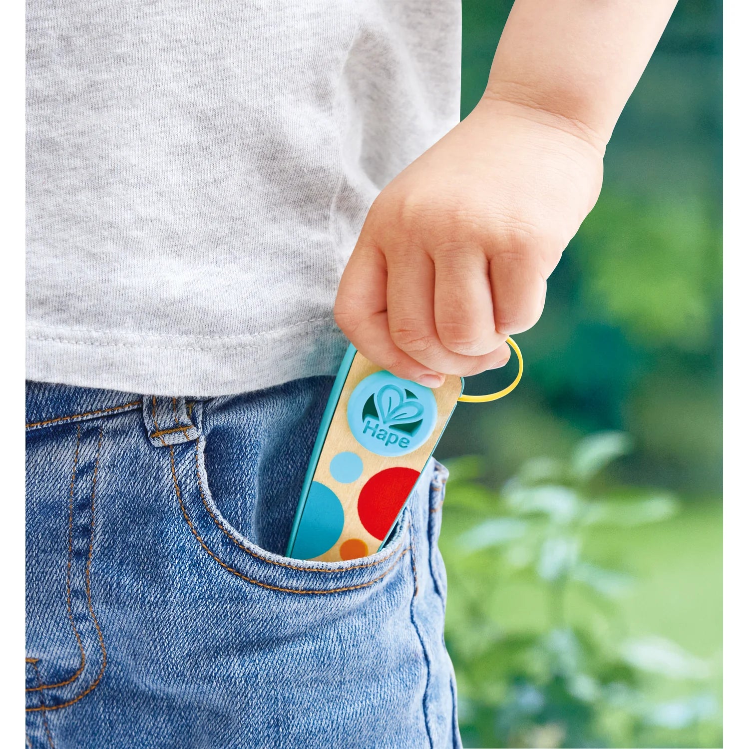 Child's hand holding a colorful Hape toy with a blurred green background
