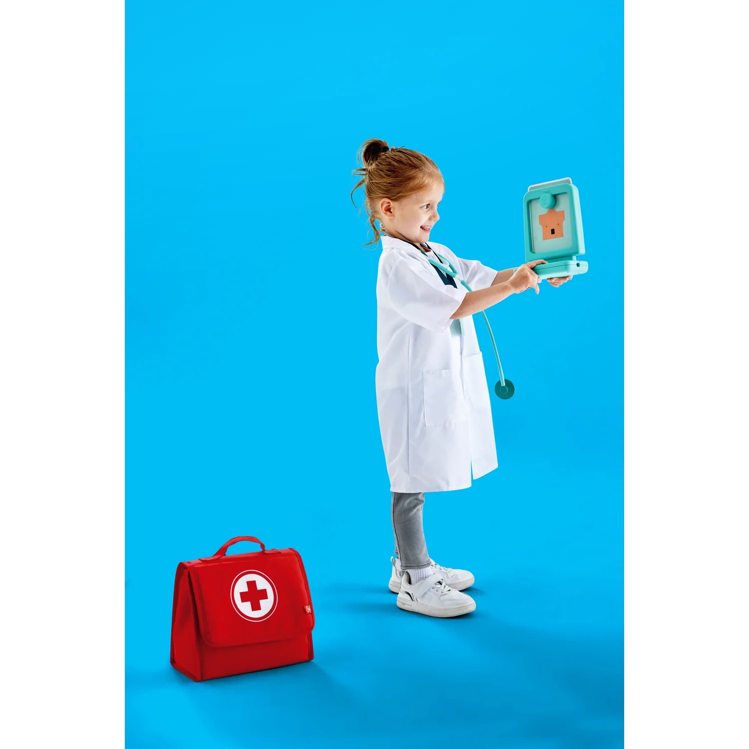Child in a white coat holding a toy stethoscope and first aid kit on a blue background