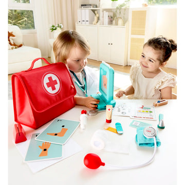 Children playing with a toy doctor set on a table, including a red first aid bag with a white cross.