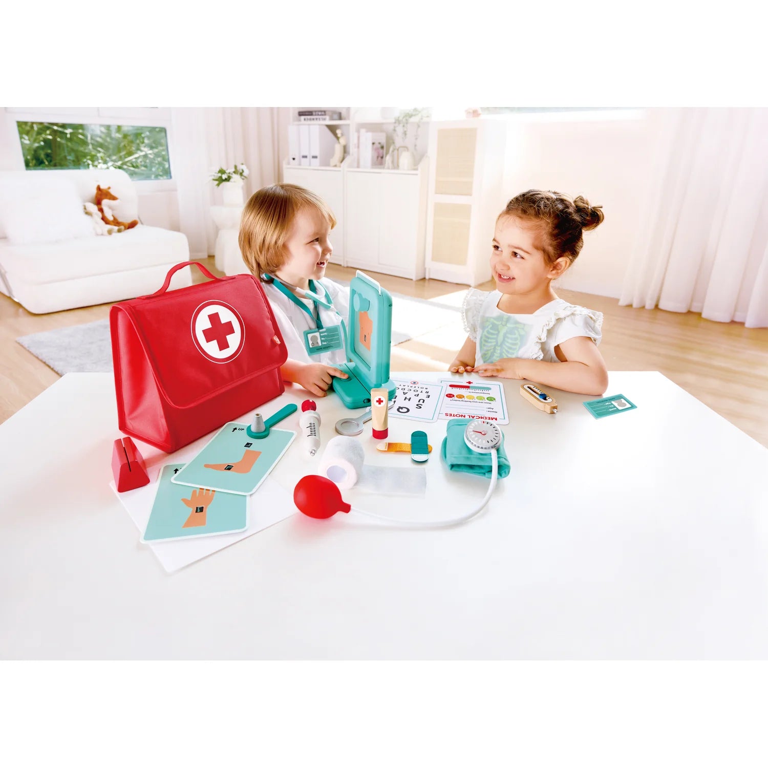 Two children playing with a toy doctor set on a table in a bright room.